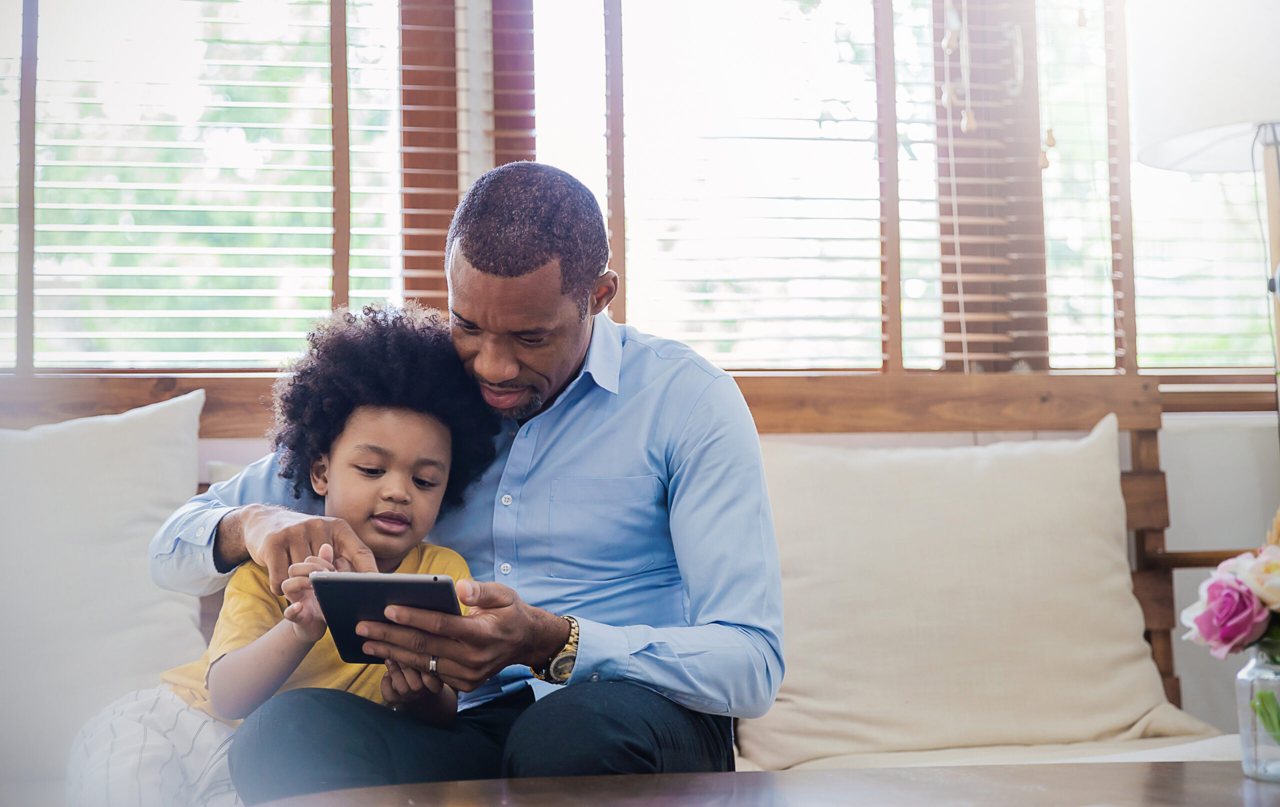 Black father and toddler son using gadget learning at home. 