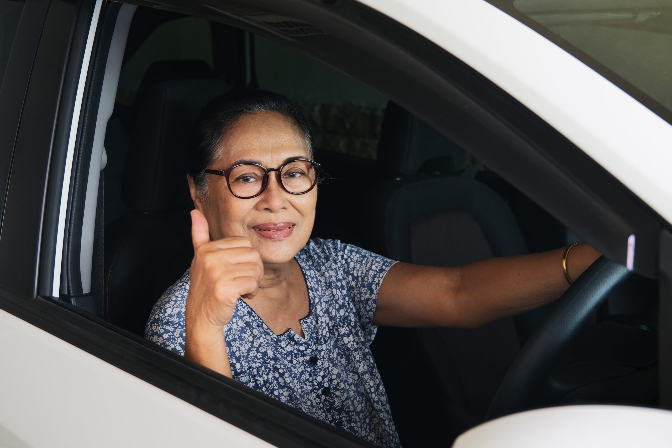 Senior Asian woman driving and giving thumbs up