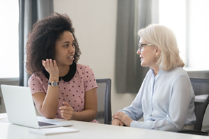 Young Black woman and senior white woman talking at a desk