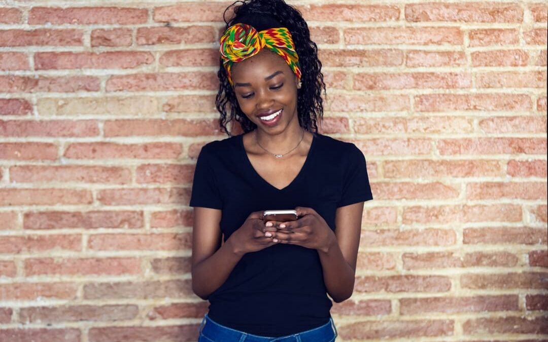 Black woman standing by brick wall using smart phone